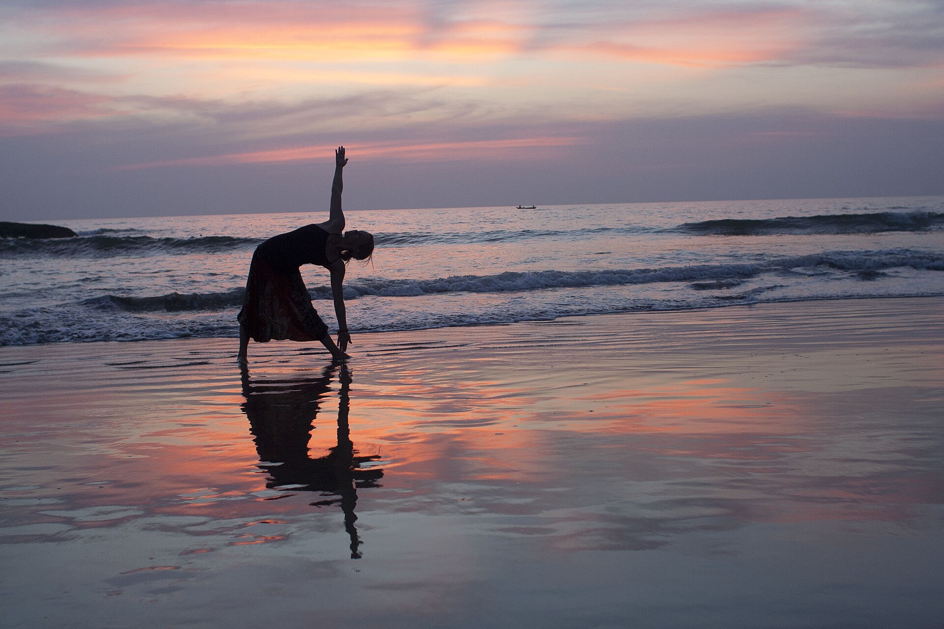 A figure silhouetted in a yoga pose on wet sand at sunset, the sky reflected around them.